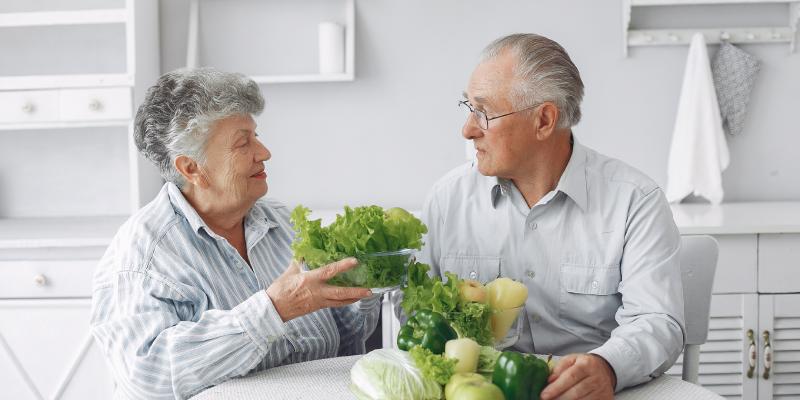 An older couple making lifestyle changes by eating vegetables in the kitchen to slow glaucoma progression.